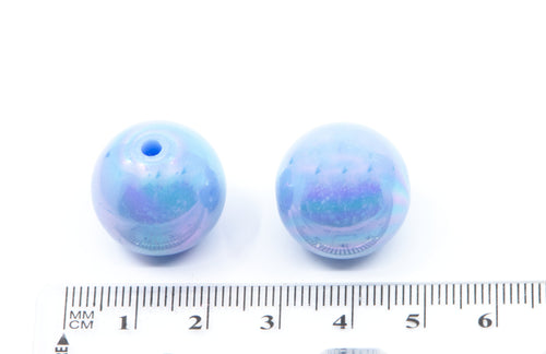 two round blue iridescent beads with a ruler for scale on a white background