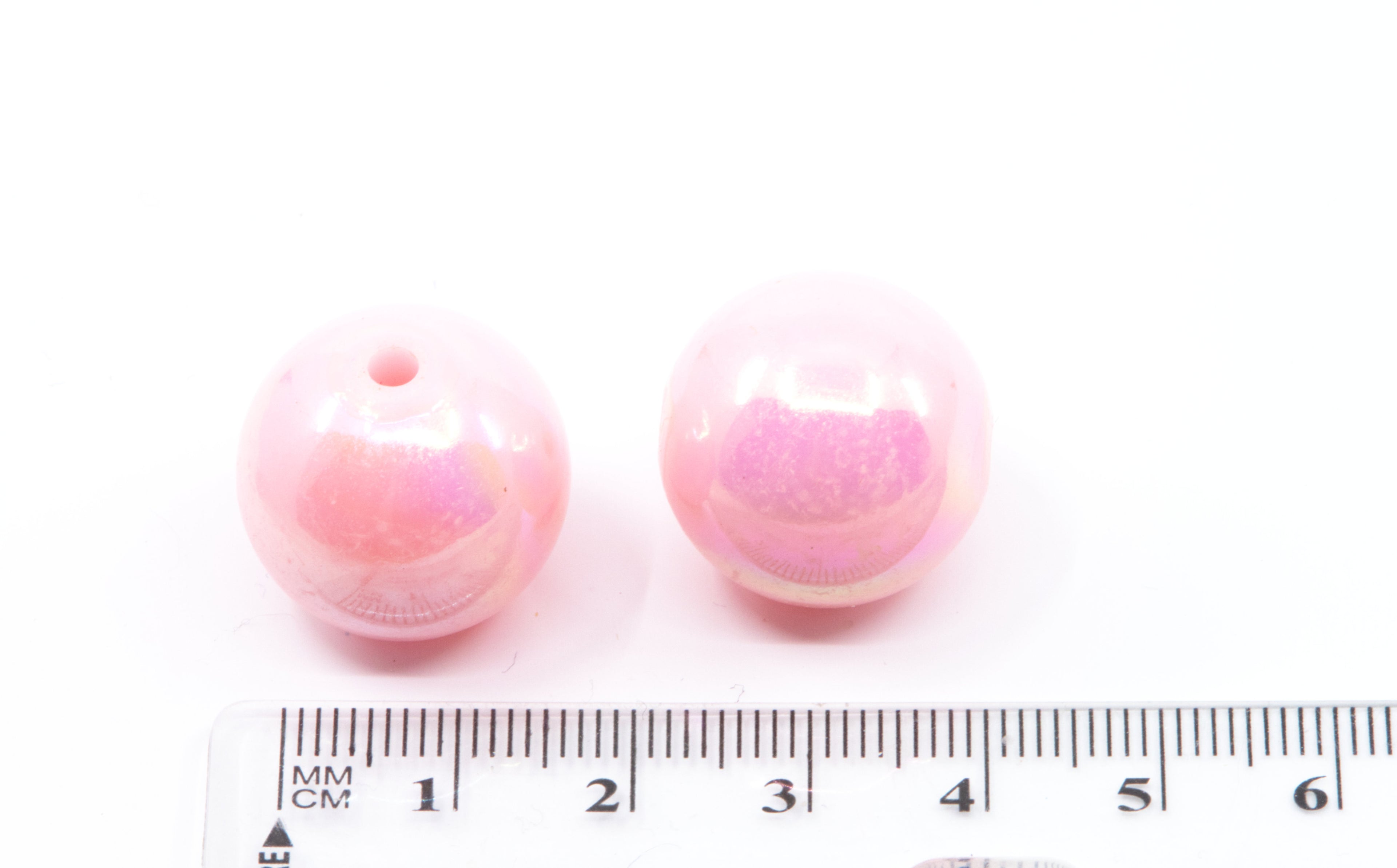 Two pink beads with a ruler for scale on a white background