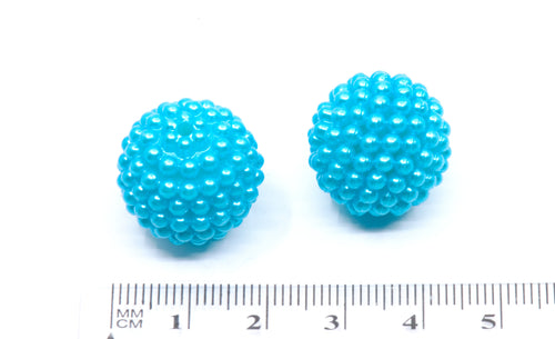 Two small round  blue textured beads shown on a white background with a centimeter ruler at the bottom for scale.