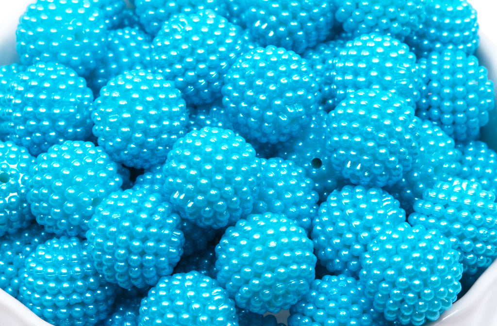 A close-up of many bright blue textured beads in a white bowl on a white background 
