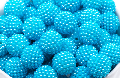A close-up of many bright blue textured beads in a white bowl on a white background 