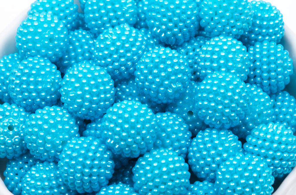 A close-up of many bright blue textured beads in a white bowl on a white background 