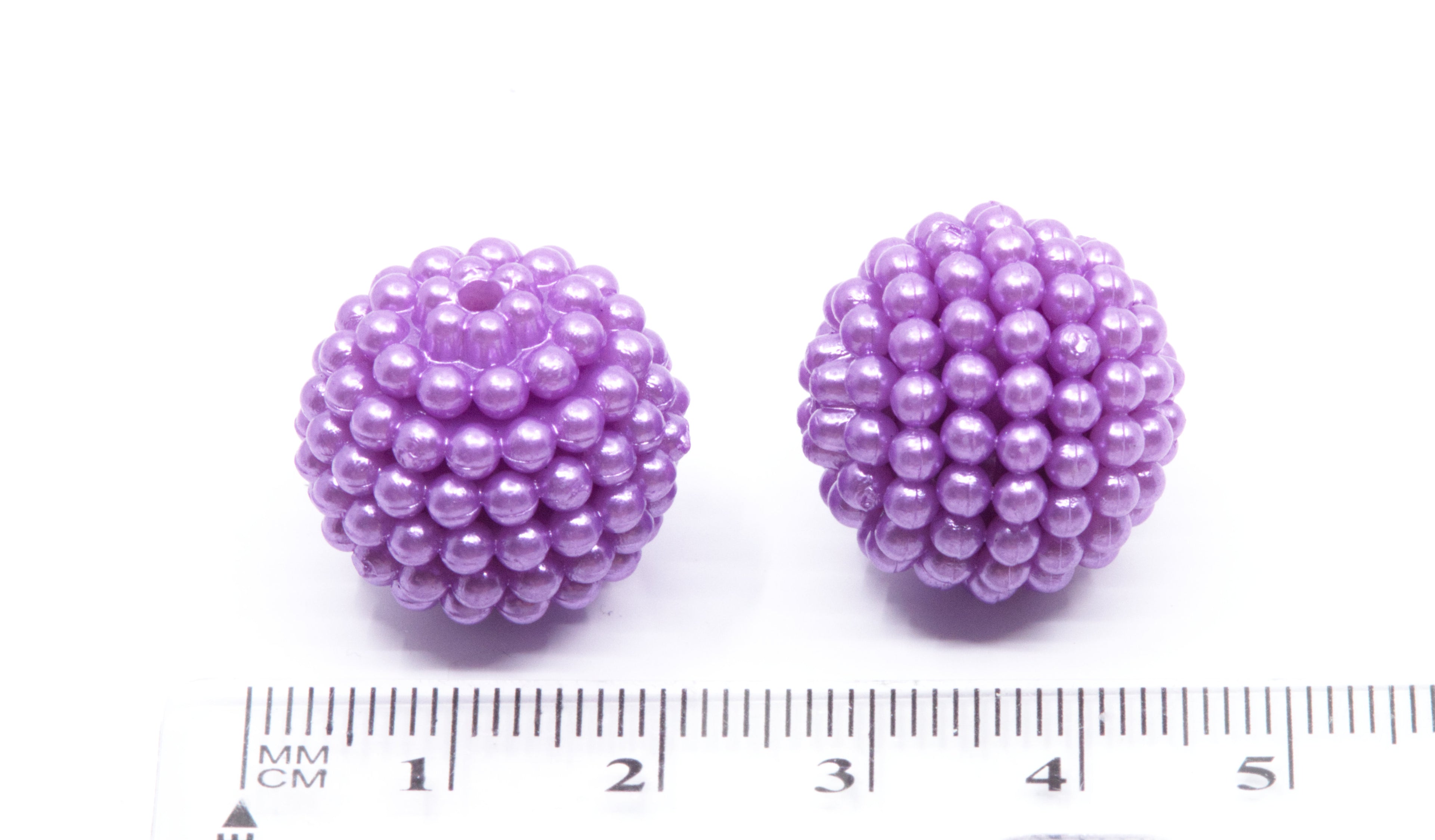 Two small spherical purple beads with a textured, beaded surface, shown next to a centimeter ruler for scale on a white background.