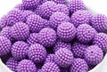 A close-up of many purple beads piled together in a white bowl against a white background.