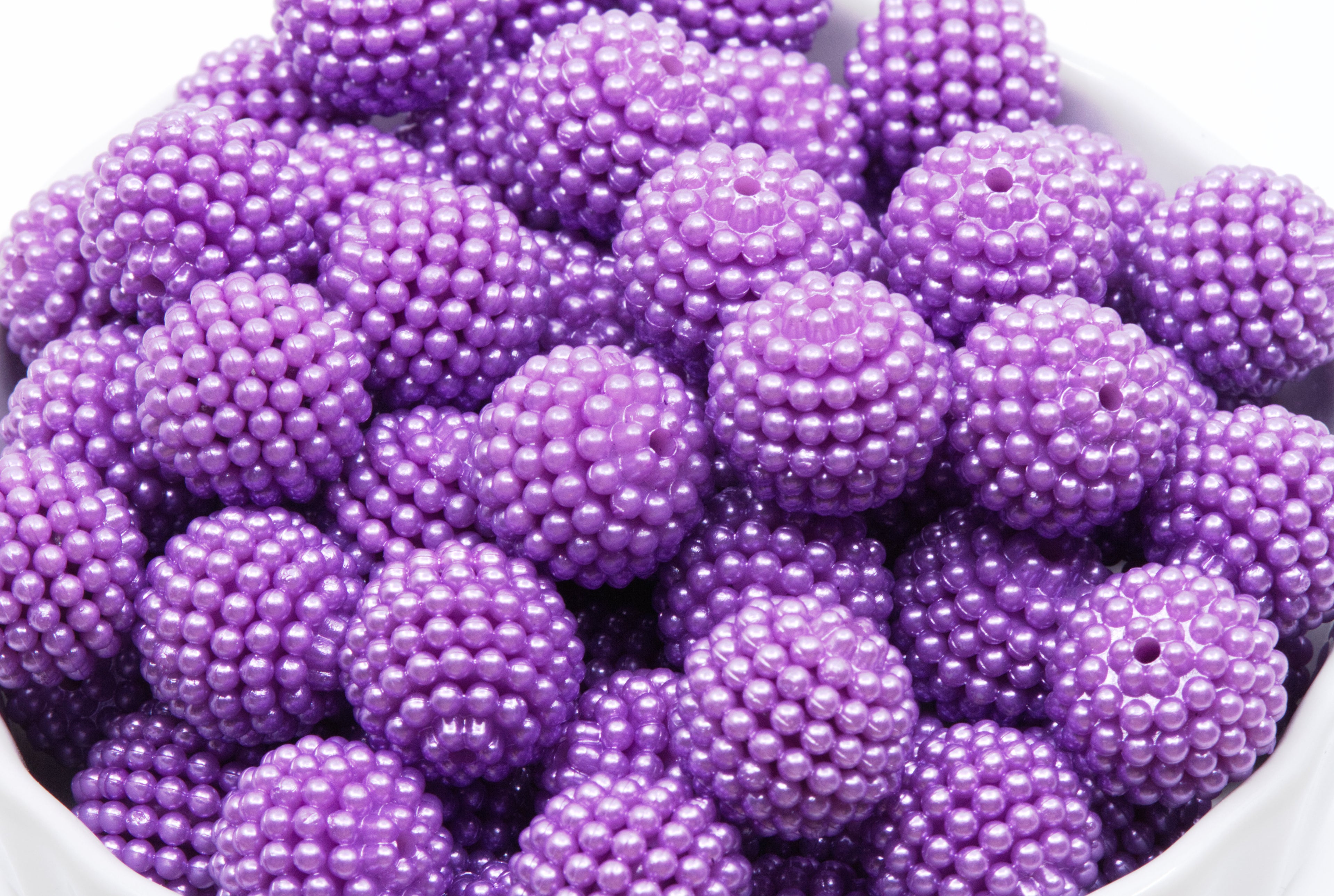 A close-up of many purple beads piled together in a white bowl against a white background.