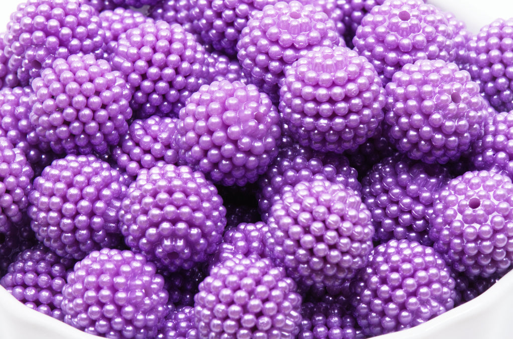 A close-up of many purple beads piled together in a white bowl against a white background.