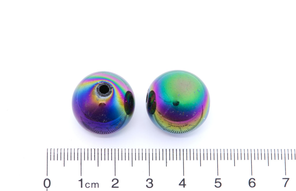 Two black iridescent beads with a ruler for scale on a white background