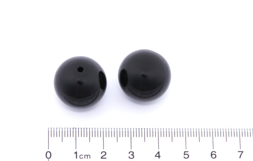 Two black beads with a ruler for scale on a white background