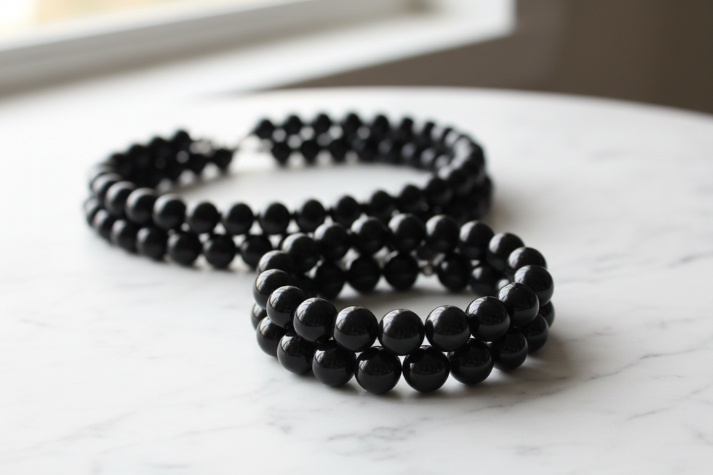 Black beads displayed as bracelets and necklaces on a marble surface