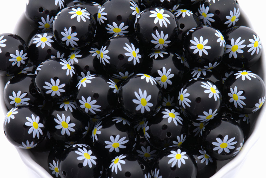 Black beads with white daisy patterns arranged in a bowl.