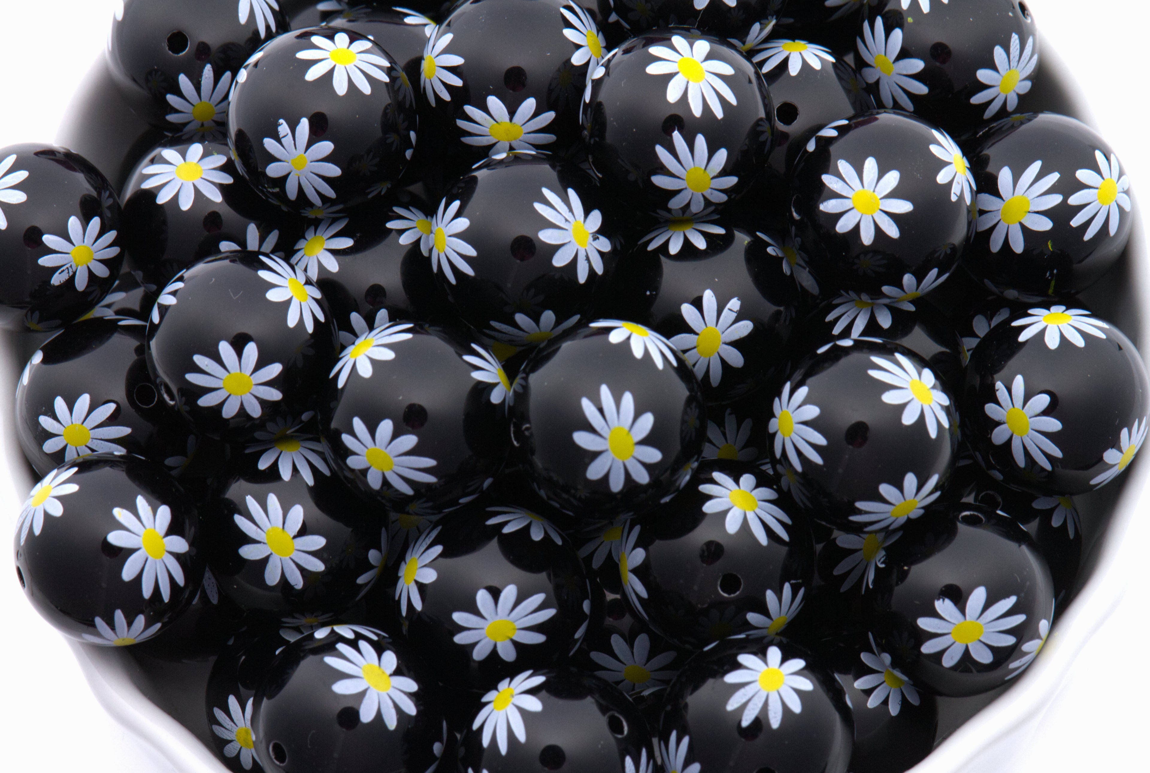 Black beads with white daisy patterns arranged in a bowl.