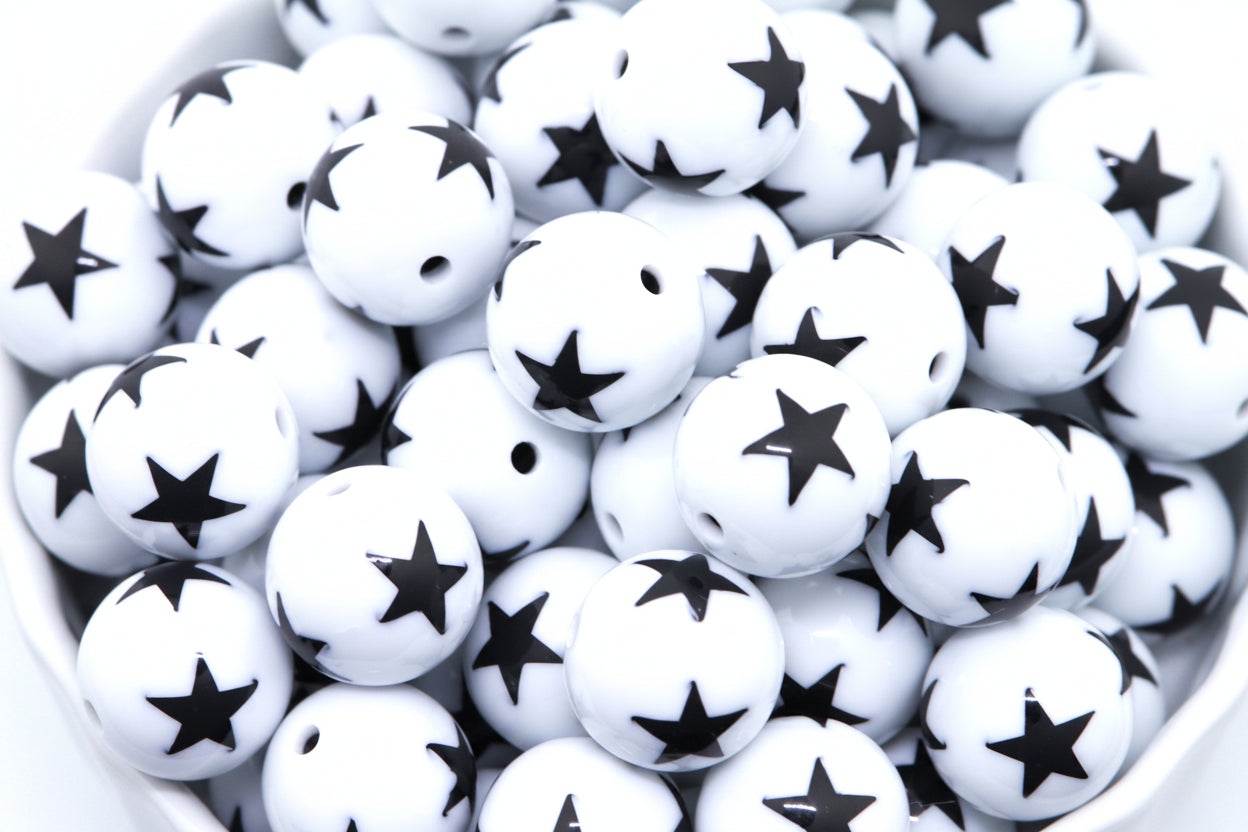 White beads with black star print, piled inside a white bowl against a white background.