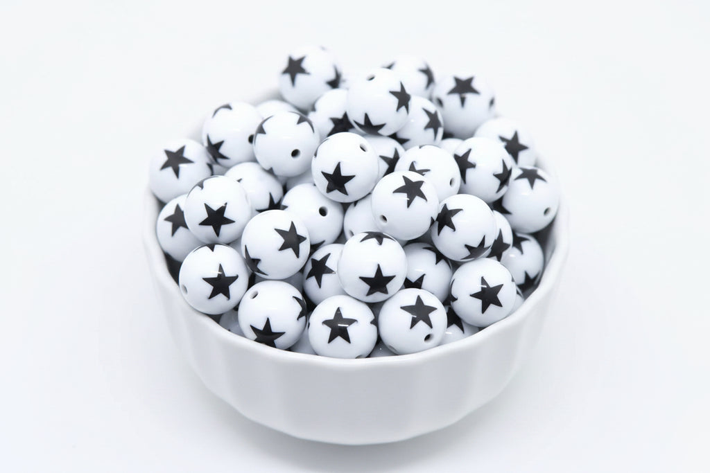 White beads with black star print, piled inside a white bowl against a white background.