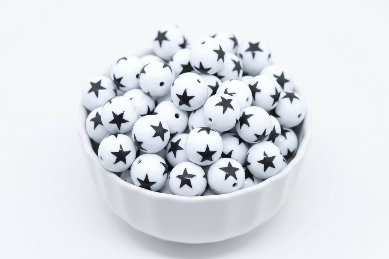 White beads with black star print, piled inside a white bowl against a white background.