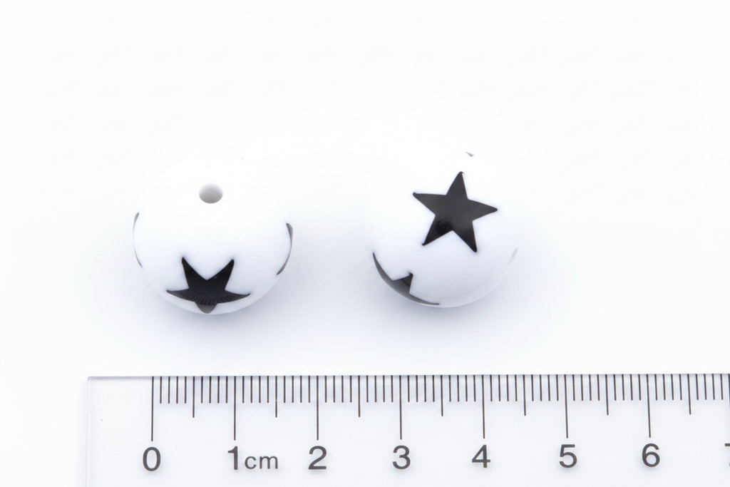 Two white round beads with black star print, shown above a cm ruler for scale on a white background.