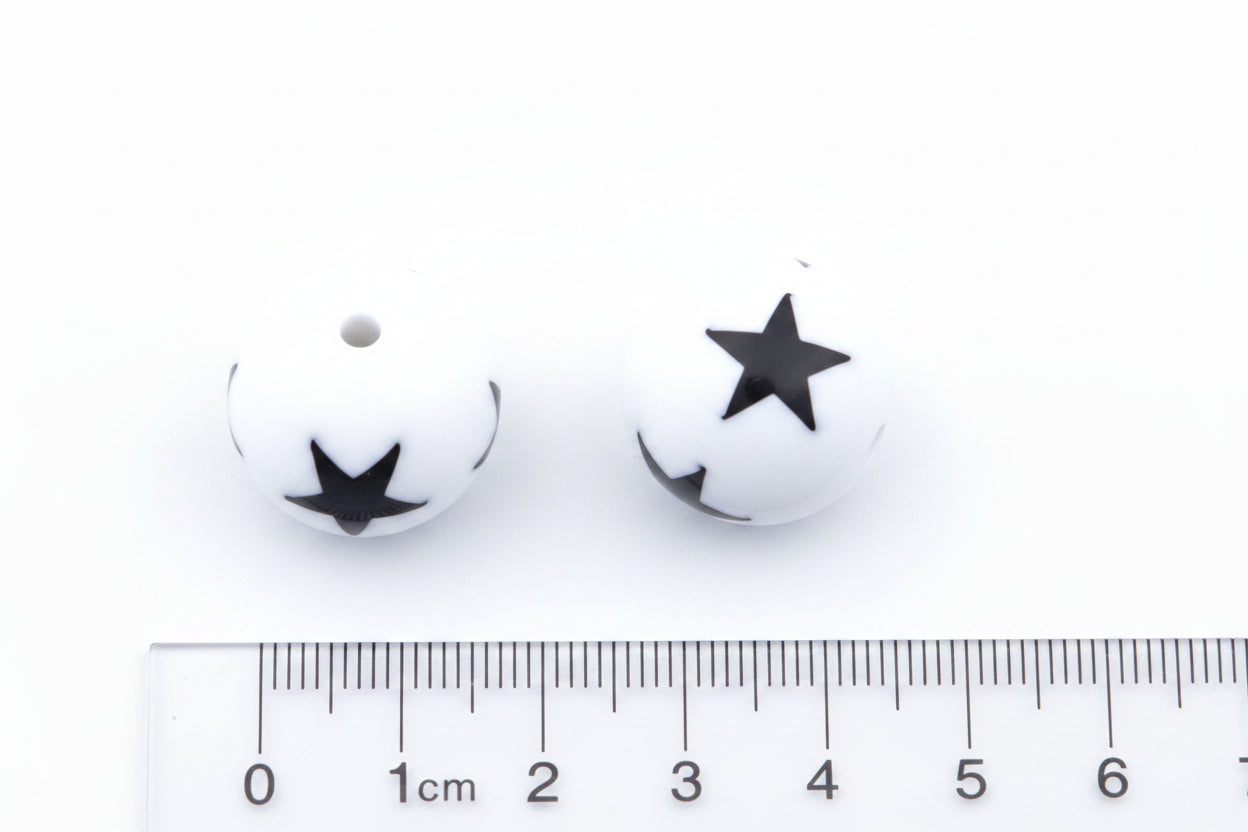 Two white round beads with black star print, shown above a cm ruler for scale on a white background.