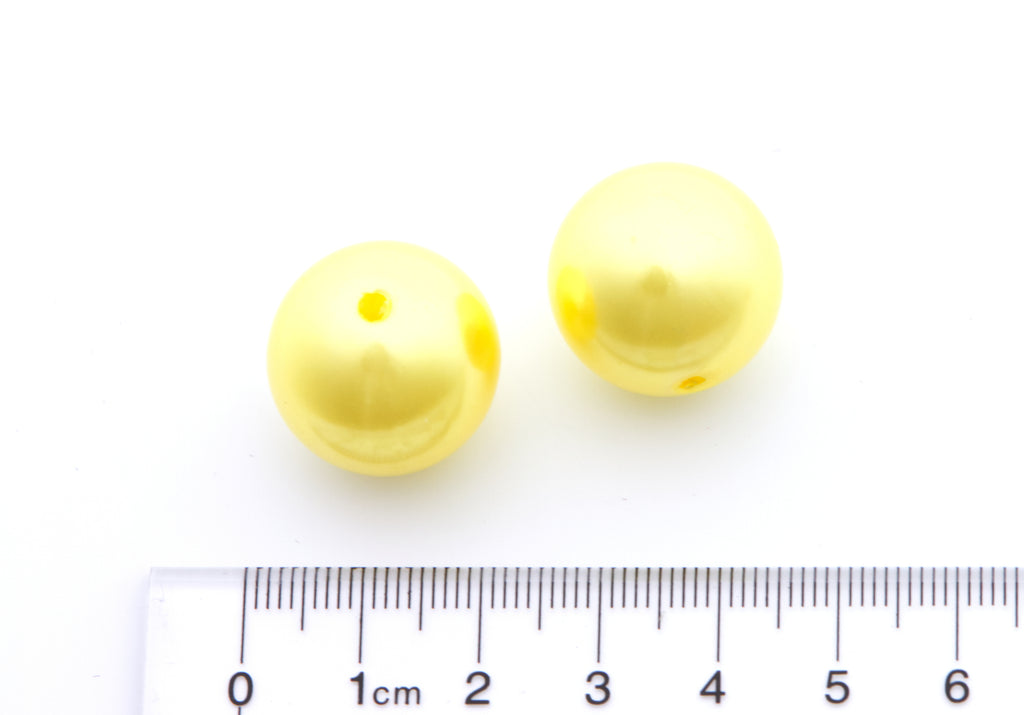 Two yellow metallic beads next to a ruler for size reference on a white background