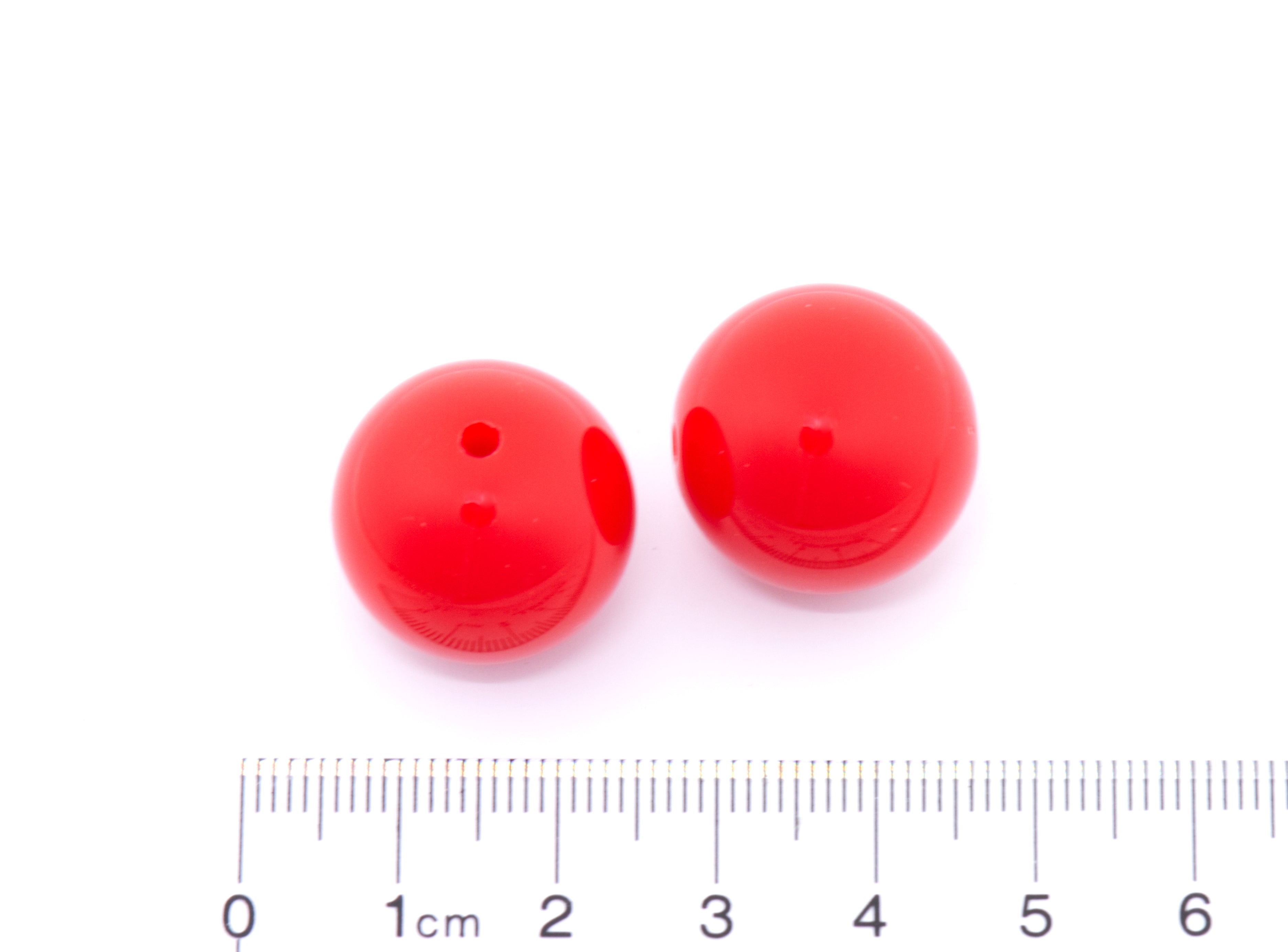 Two red beads with a ruler for scale on a white background