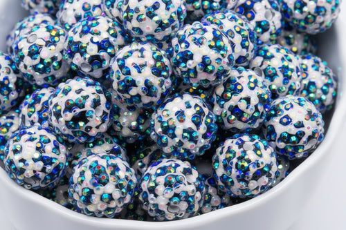 A close-up of many round black and white cheetah print rhinestone beads, piled inside a white bowl.