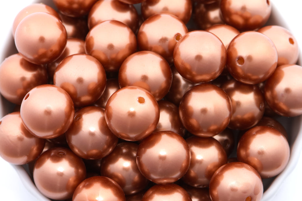 A close-up of shiny metallic copper brown beads piled in a white ceramic bowl. 