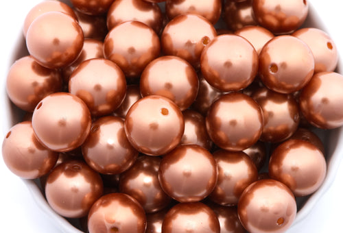 A close-up of shiny metallic copper brown beads piled in a white bowl, with the beads filling almost the entire frame.