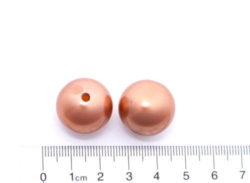 Two metallic copper brown round beads with a central hole, shown next to a centimeter ruler for scale on a white background.