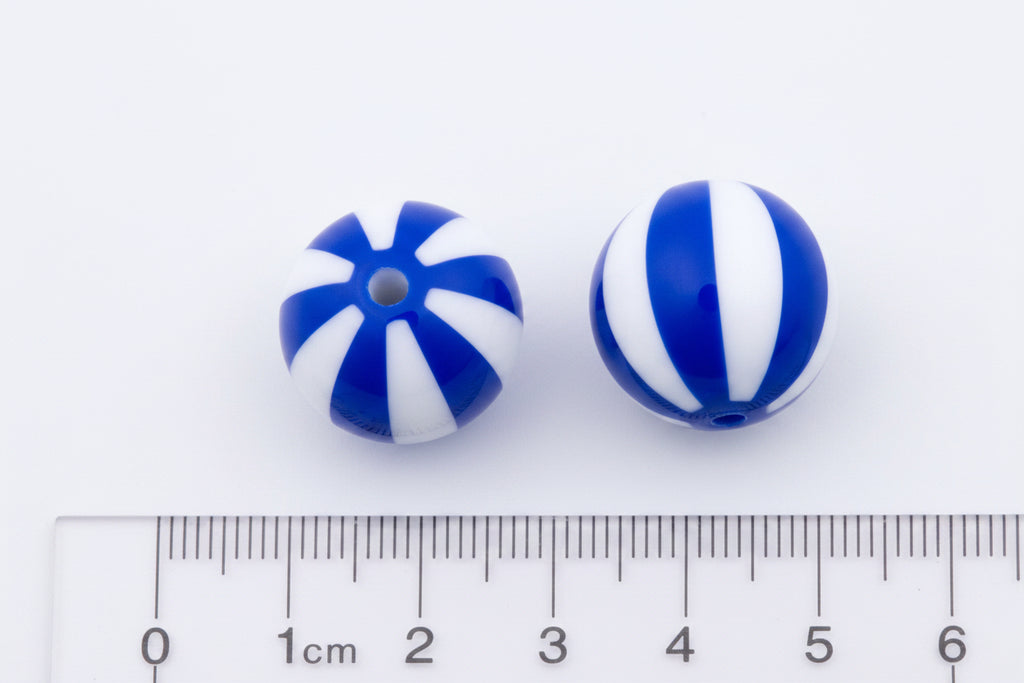Two round bubblegums beads with blue and white striped patterns, shown next to a cm ruler on a black background.