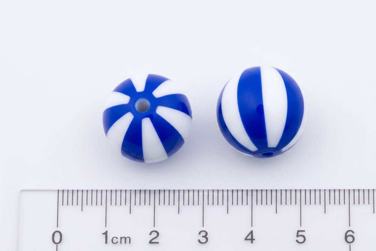 Two round bubblegums beads with blue and white striped patterns, shown next to a cm ruler on a black background.