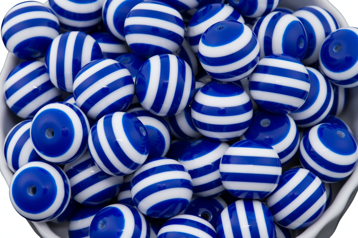 A close-up of many round beads with blue and white horizontal stripes, piled inside a white bowl.