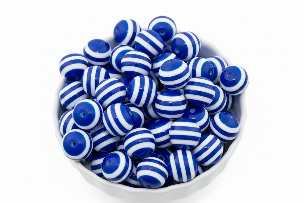 A white bowl filled with glossy blue and white striped round beads on a plain white background.