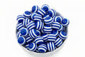 A white bowl filled with glossy blue and white striped round beads on a plain white background.