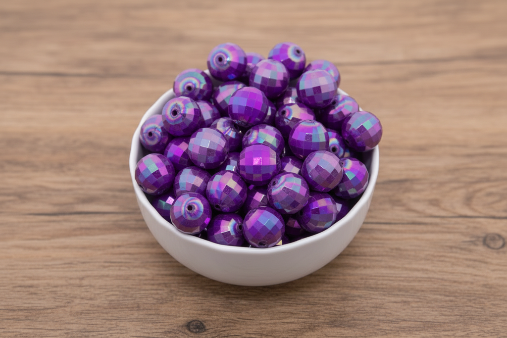 Purple faceted beads in a white bowl on a wooden surface
