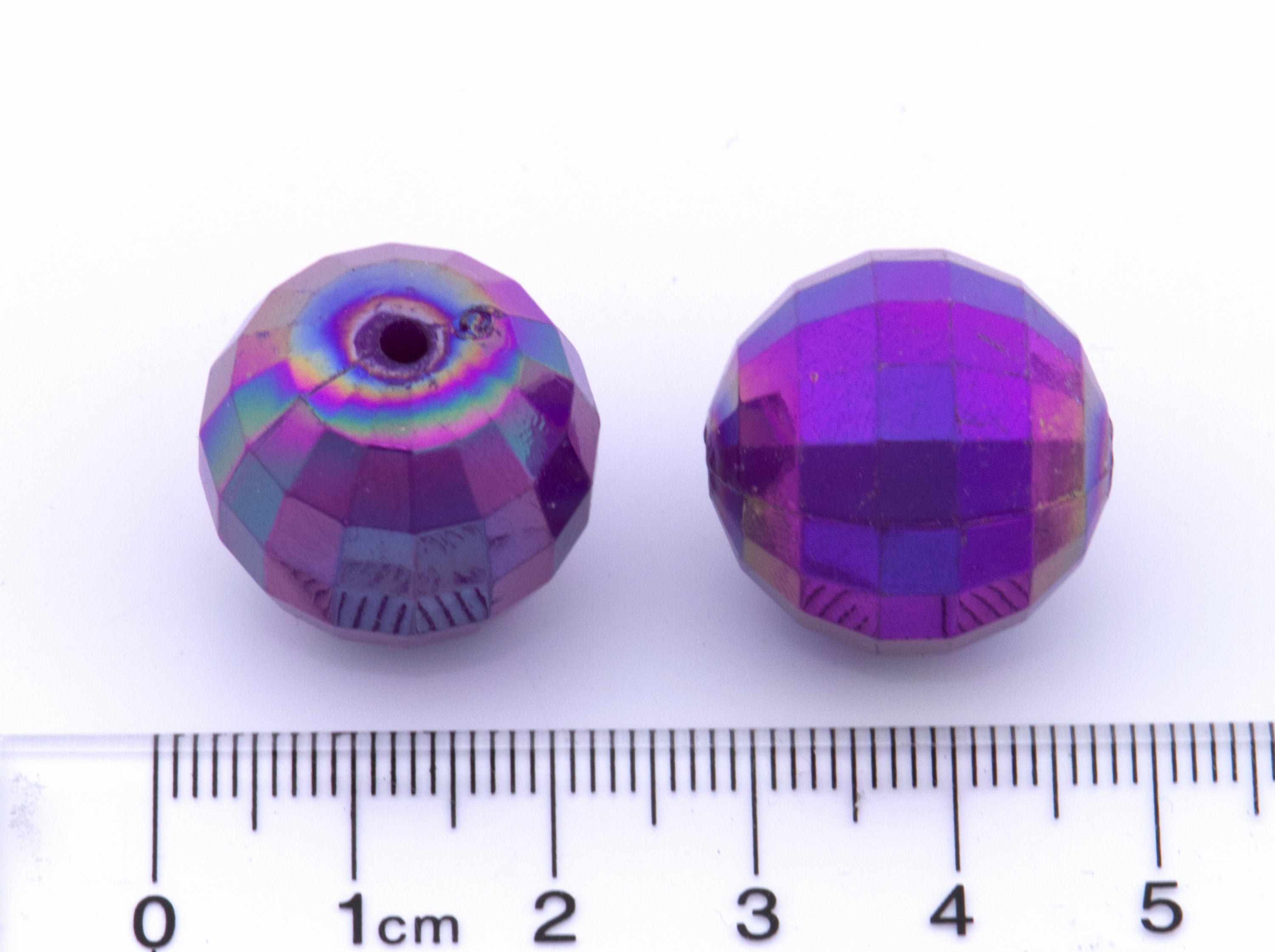 Two purple faceted beads with a ruler for scale on a white background