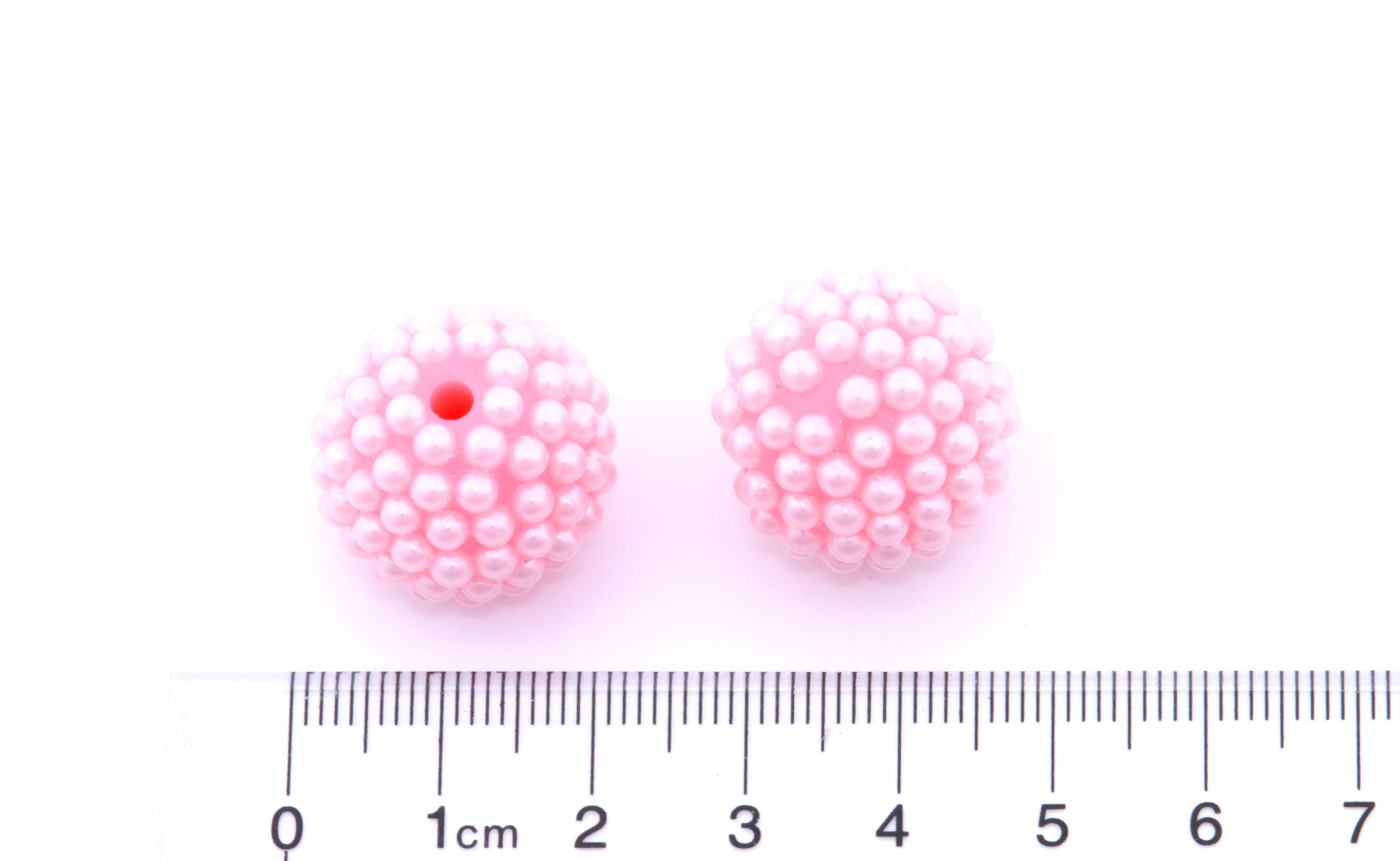 Pink pearl-like beads with a ruler for scale on a white background