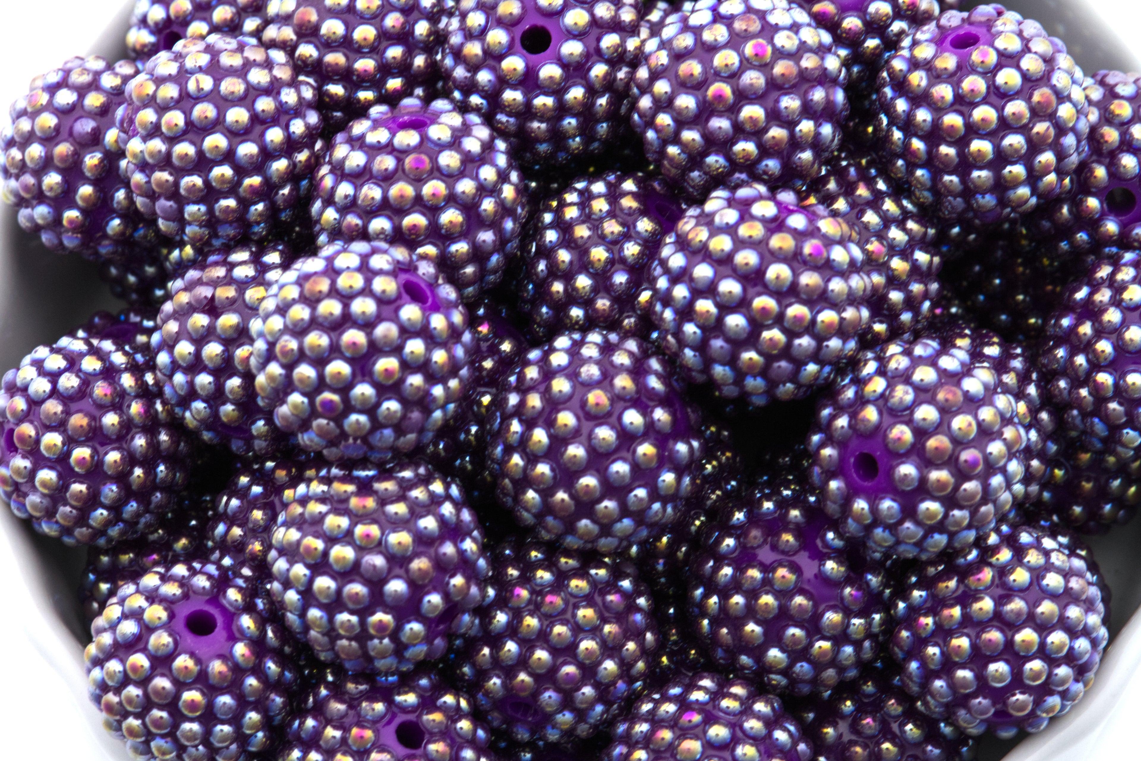 Close-up of purple beads with AB coating in a white bowl on a white background 