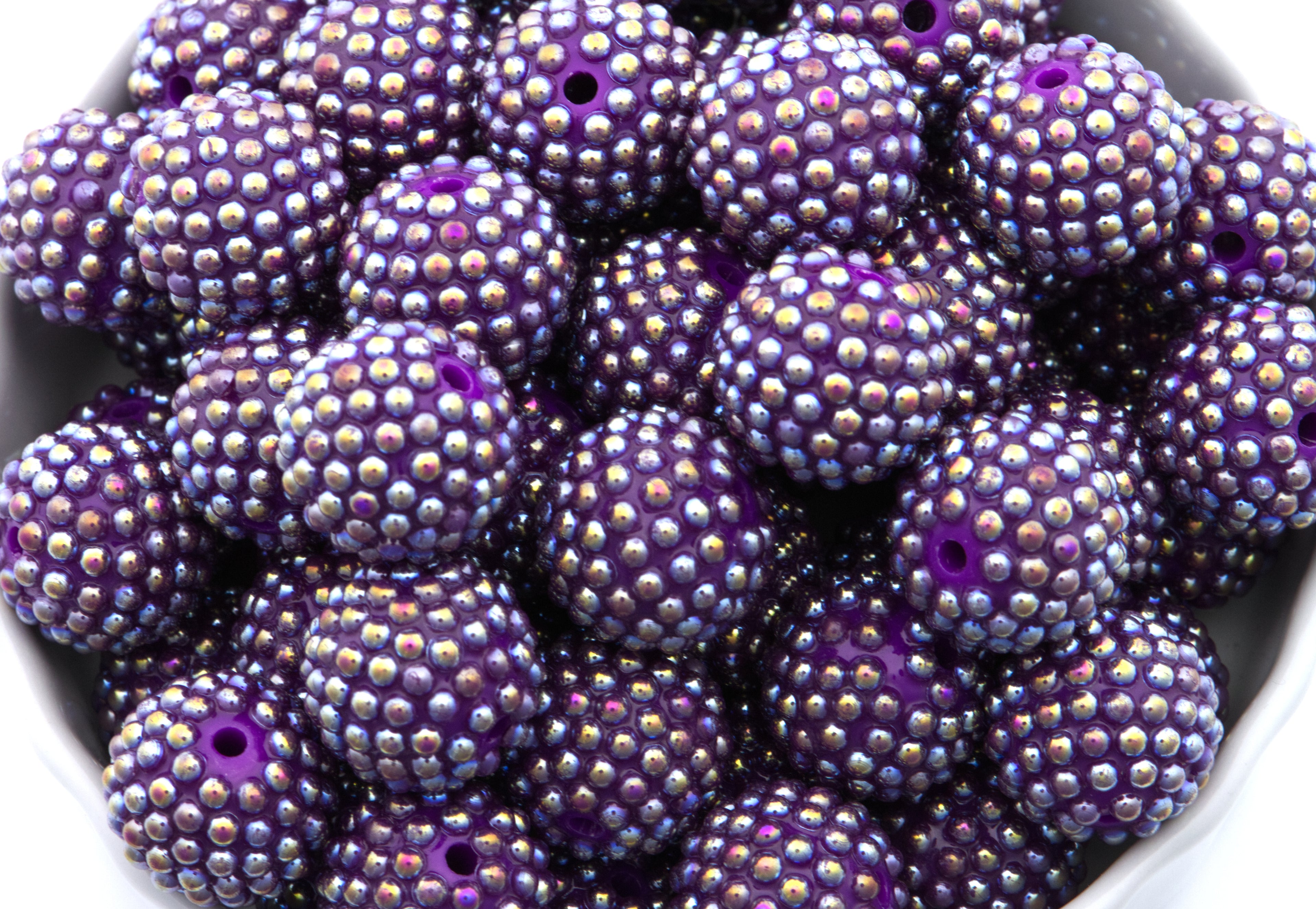 Purple beads with an AB coating in a white bowl on a white background 