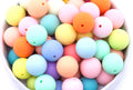 A close-up of round frosted matte rainbow beads in multiple colors, including pink, blue, yellow, orange, mint green, and purple, piled inside a white bowl.