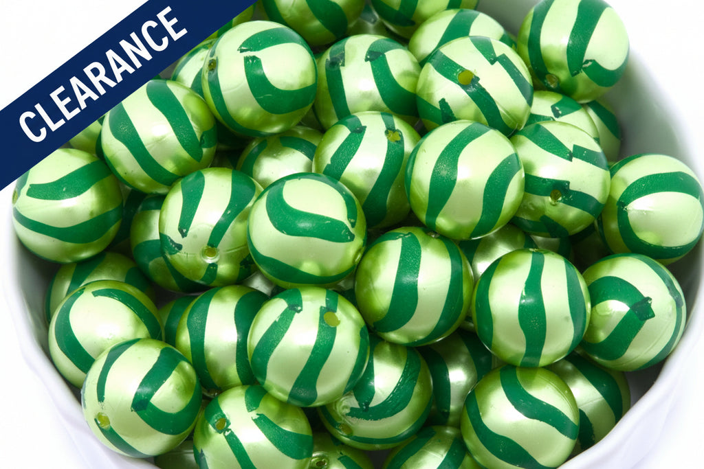 Close up of green striped metallic beads in a white bowl on a white background. clearance label on top left corner 