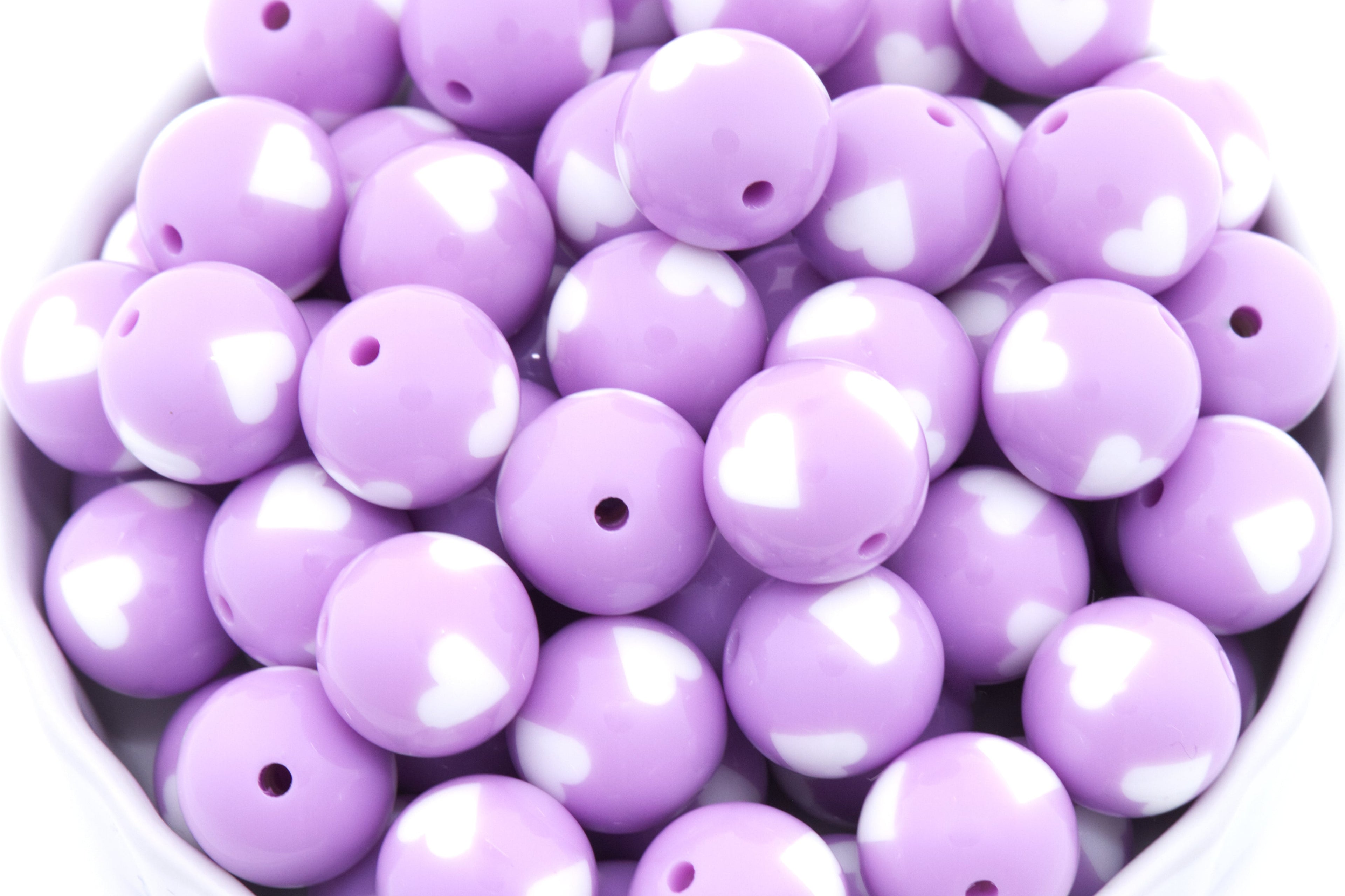 Purple beads with white heart patterns in a white bowl