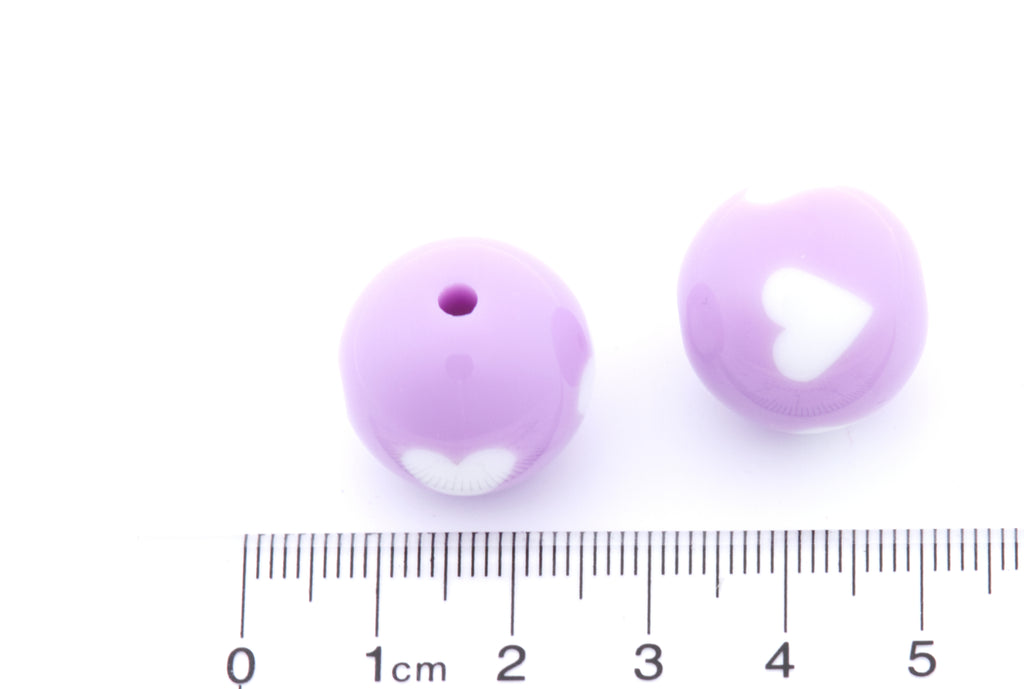 Two purple beads with white hearts on a white background, accompanied by a ruler for scale.