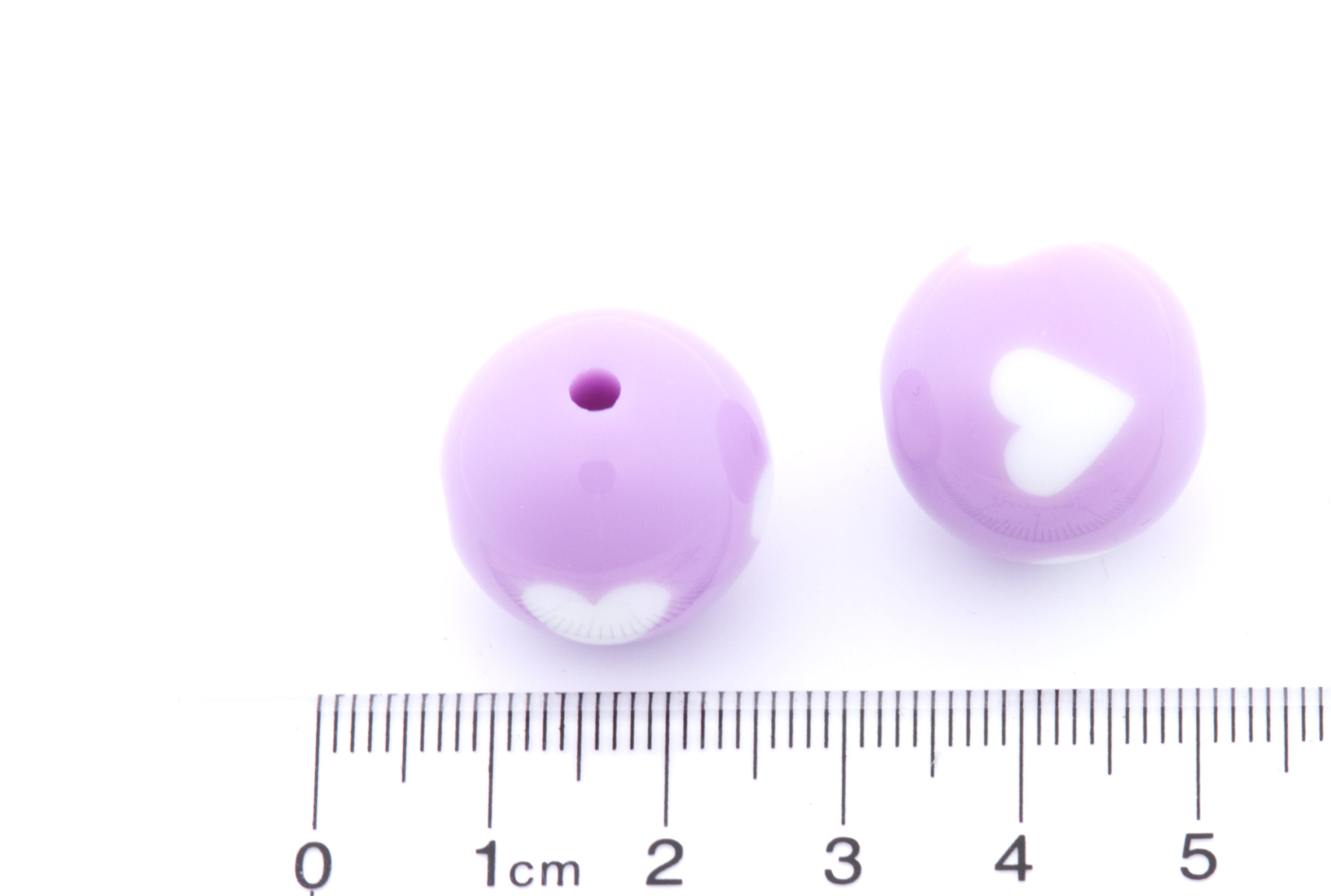 Two purple beads with white hearts on a white background, accompanied by a ruler for scale.