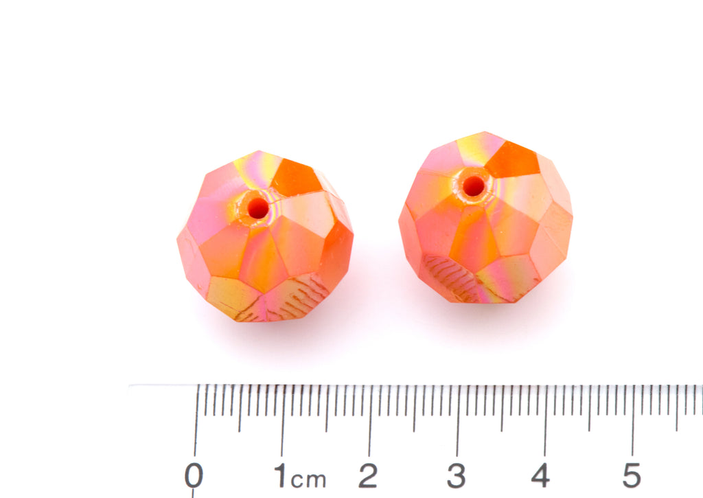 two orange faceted beads next to a ruler for size reference on a white background