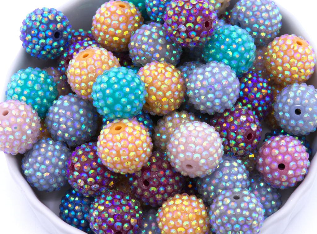 Colorful rhinestone beads with iridescent finish in a white bowl on a white background 