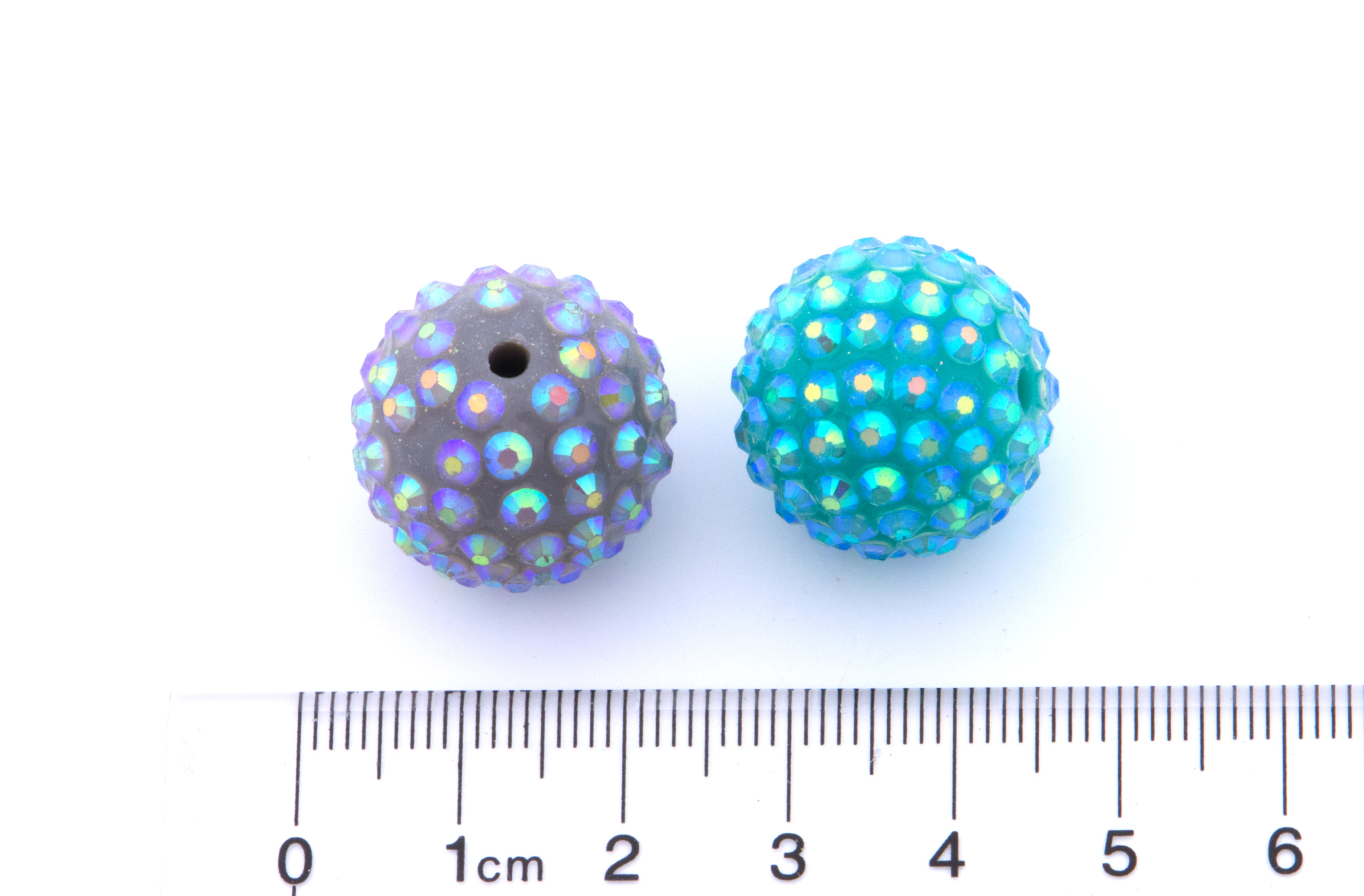 Two colorful rhinestone beads next to a ruler on a white background