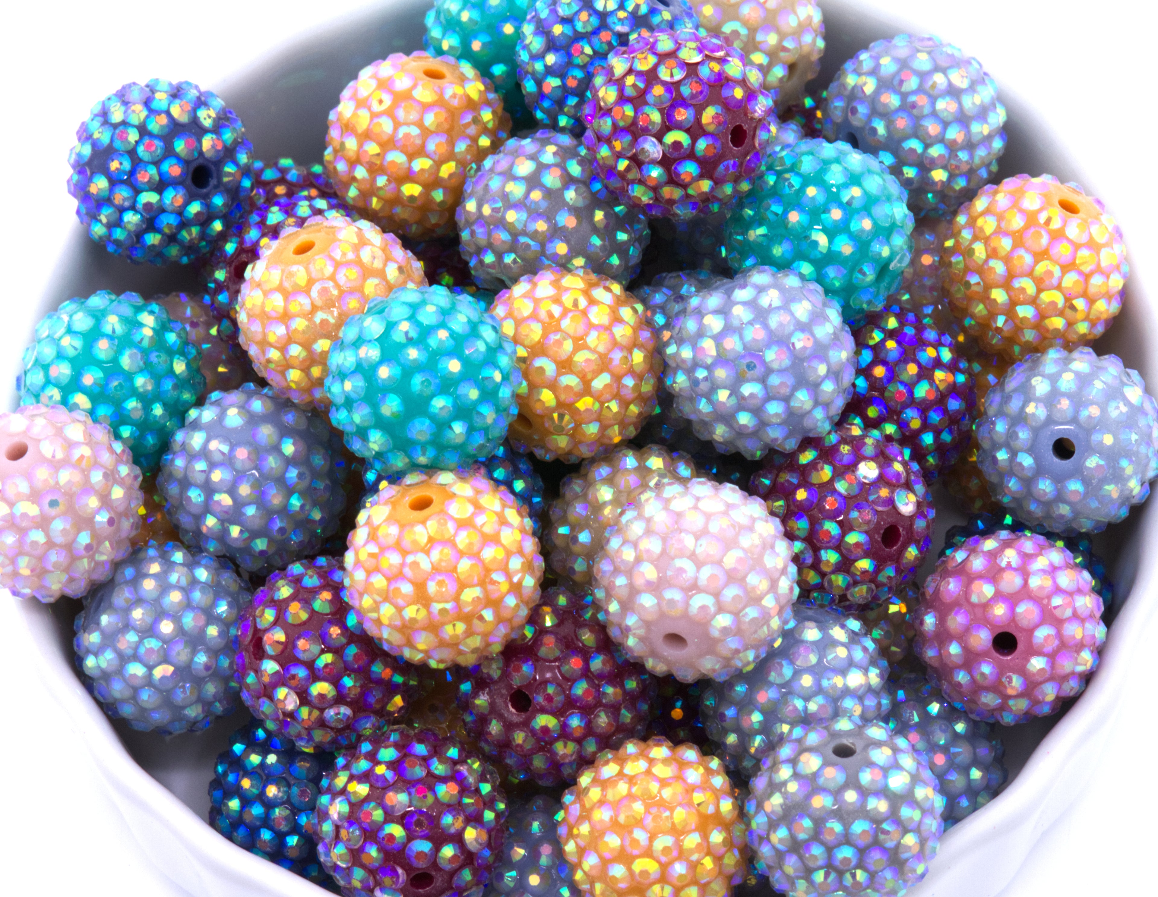 Colorful rhinestone beads with a  iridescent finish in a white bowl on a white background