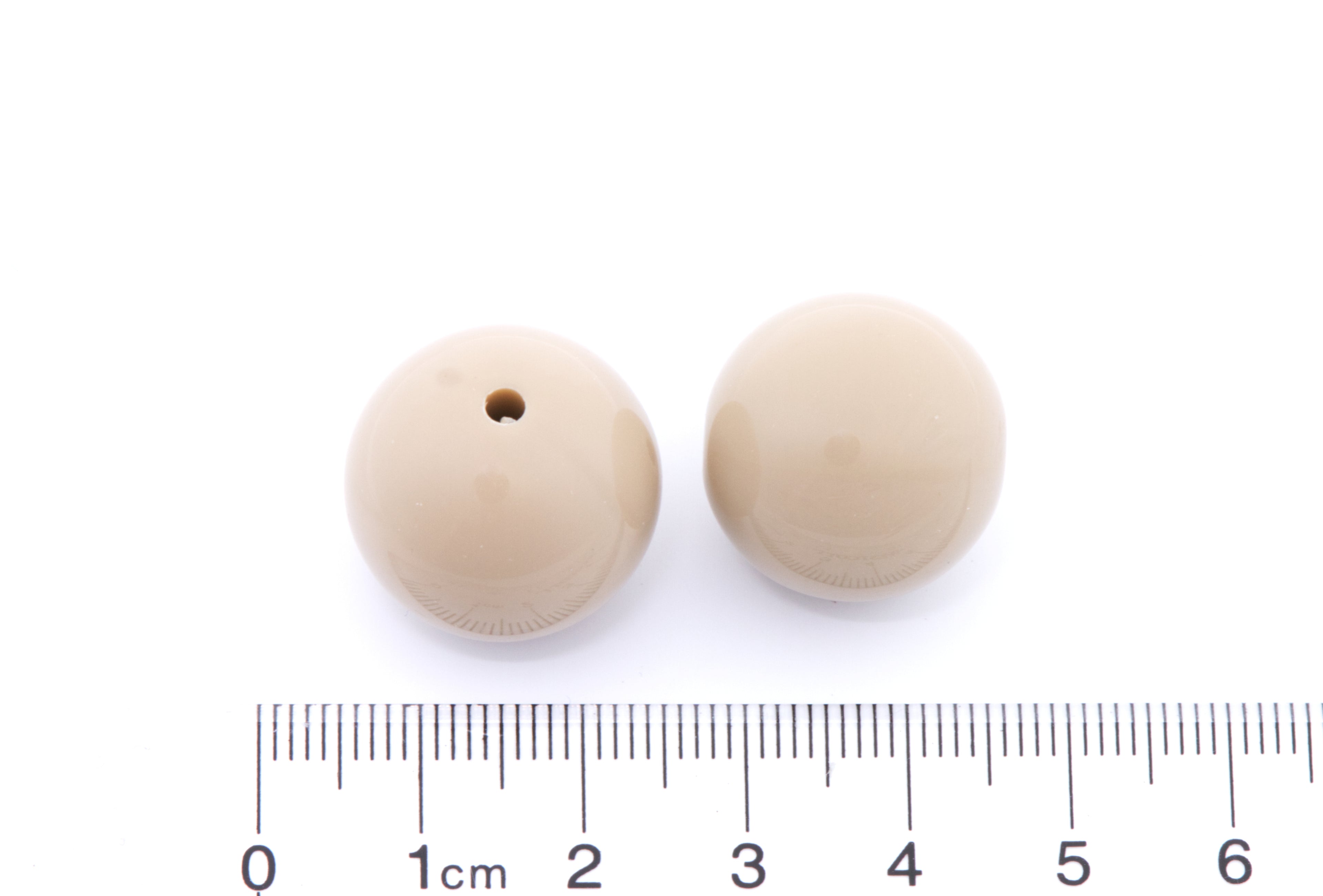 Two brown beads with a ruler for scale on a white background