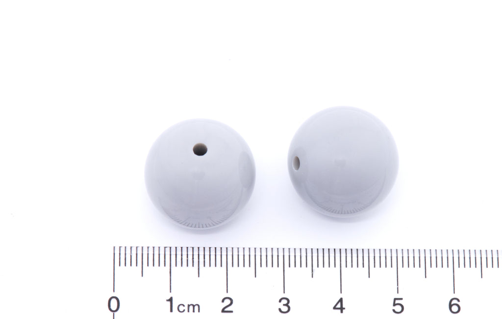 Two gray beads with a ruler for scale on a white background