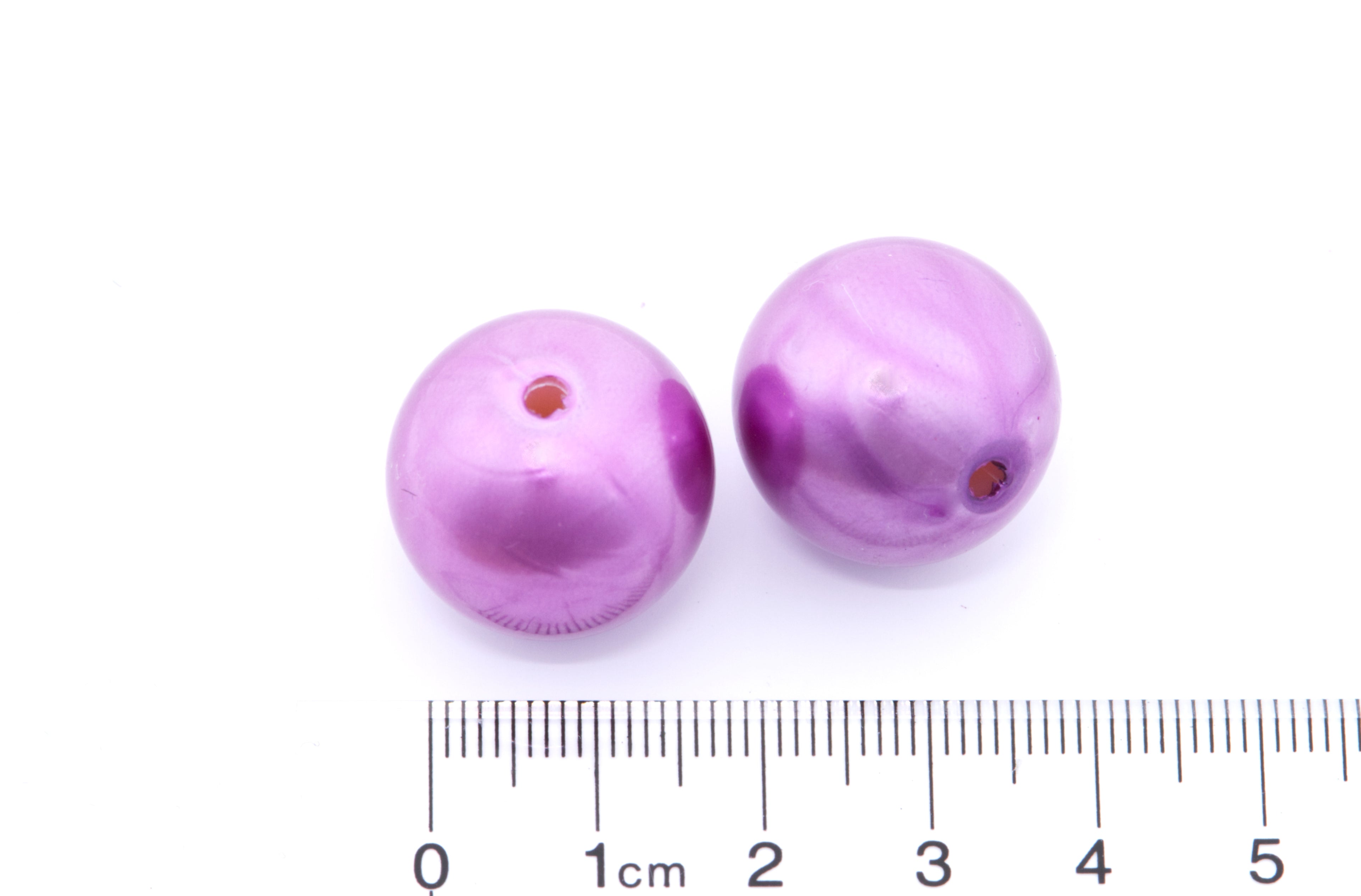 two purple bubblegum beads next to a ruler for scale on a white background