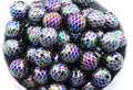 A pile of round iridescent beads with a mermaid scale pattern shown in a close-up view inside a white bowl on a white background. 