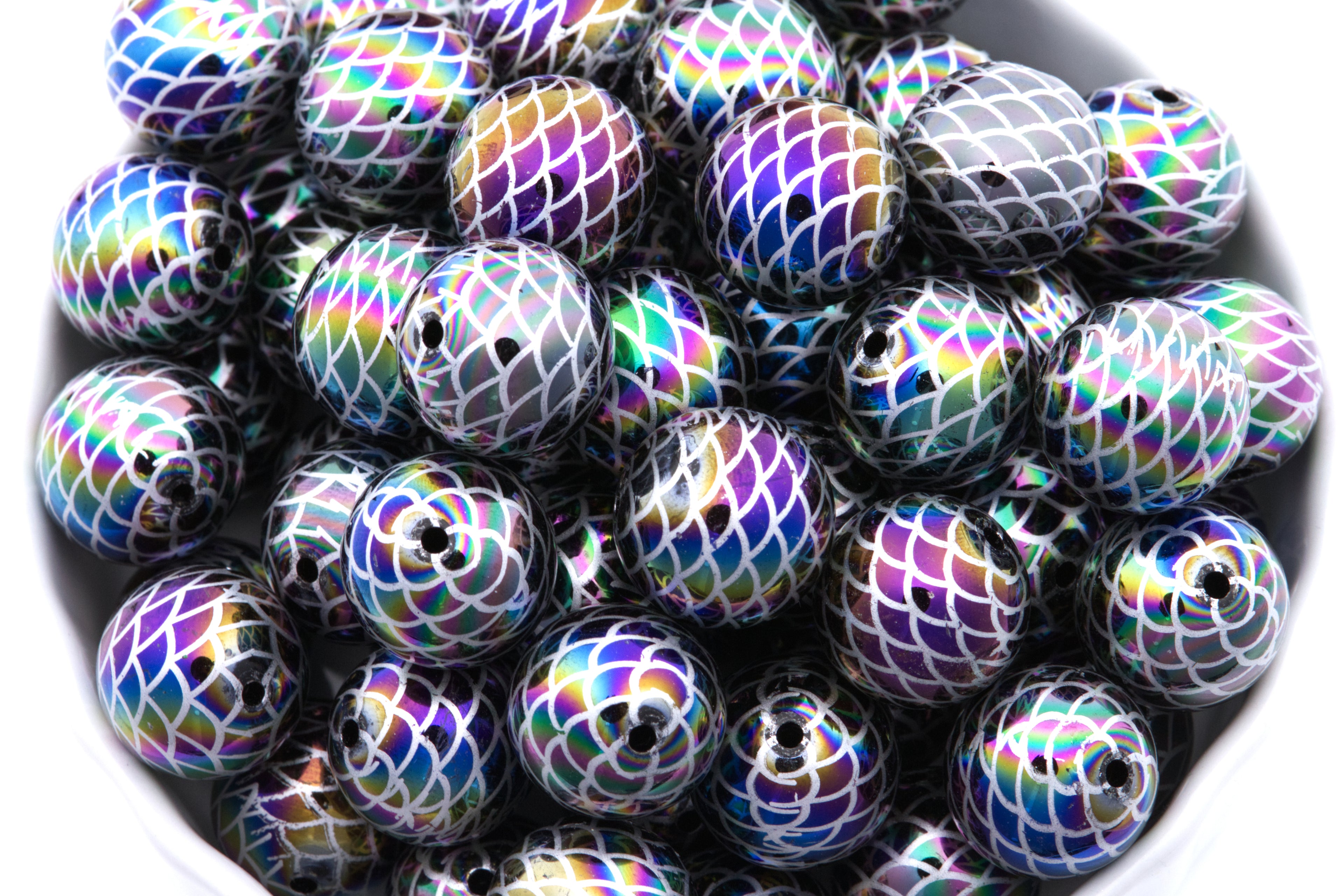 A pile of round iridescent beads with a mermaid scale pattern shown in a close-up view inside a white bowl on a white background. 